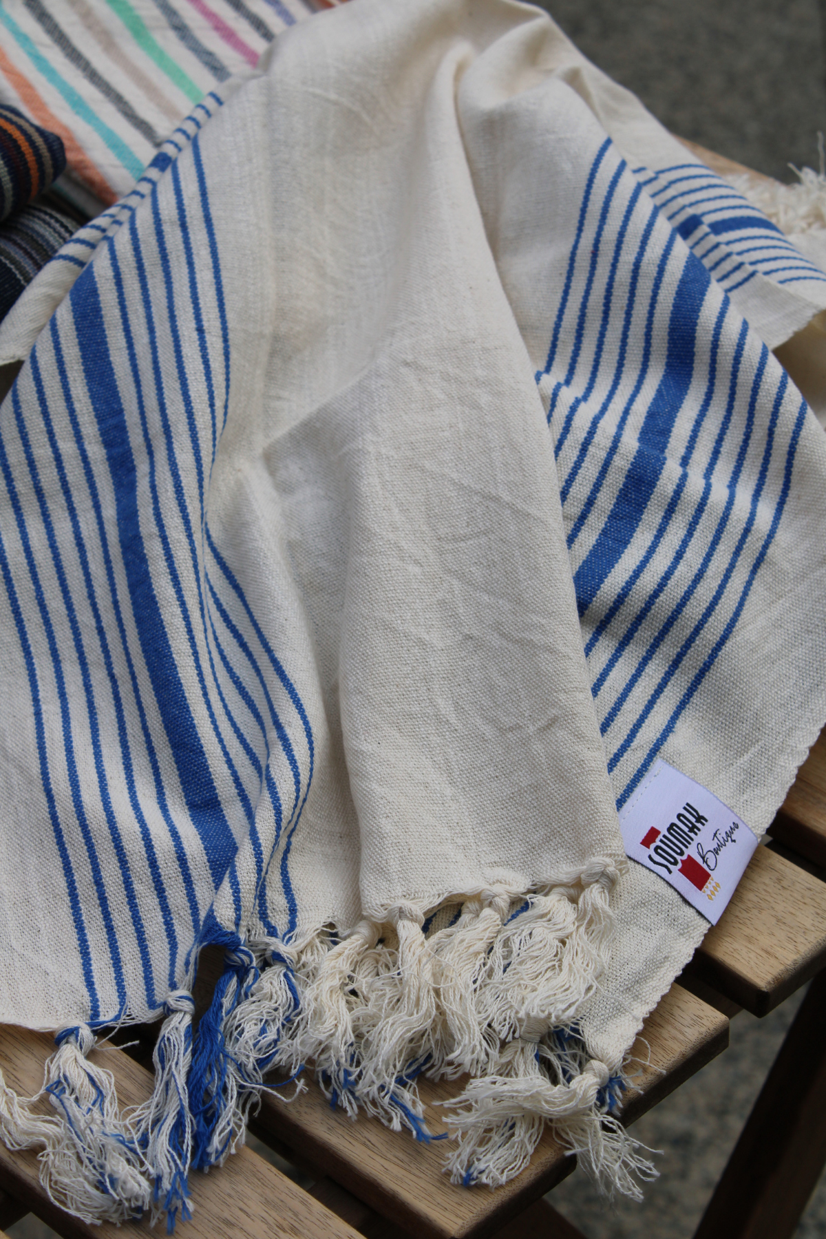 Discover the charm of our Organic Turkish Hand Towel showcased as a stylish throw on the table. Featuring elegant tassels and a high-quality design in white with blue stripes, this versatile towel is available at Soumak Boutique, Vancouver, BC, Canada, inside the Kids Market on Granville Island.